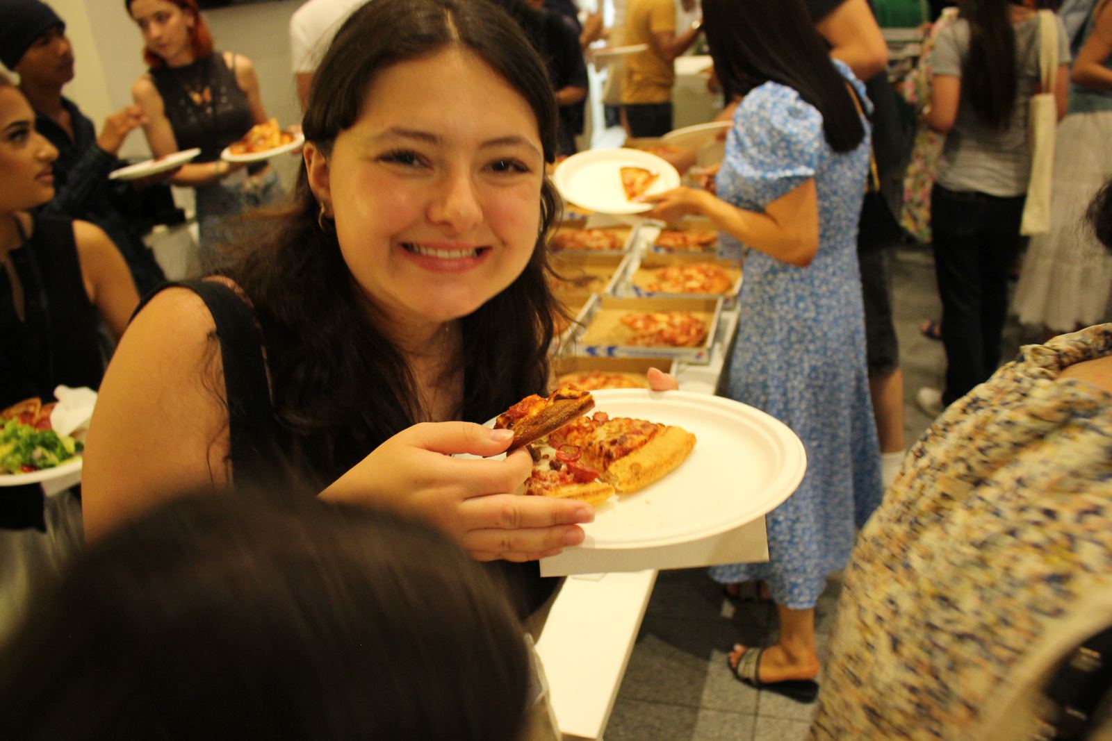 A young woman grinning with a plate of pizza at dinner